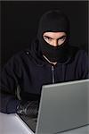 Burglar sitting hacking laptop while looking at camera on blakc background