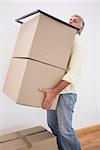 Man balancing heavy cardboard boxes at home in the living room