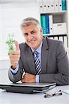 Smiling businessman showing thumbs up in his office