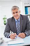 Smiling businessman writing on clipboard in his office