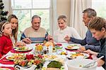 Extended family saying grace before christmas dinner at home in the dining room