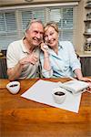 Senior couple on the phone together at home in the kitchen