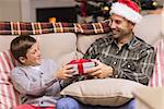 Son giving father a christmas gift on the couch at home in the living room