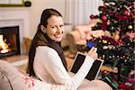 Smiling brunette shopping online with laptop at christmas at home in the living room
