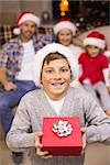 Festive son holding gift in front of his family at home in the living room