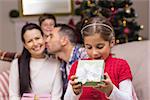 Surprised little girl opening a gift in front of her family at home in the living room