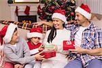 Festive family in santa hat exchanging gifts at home in the living room