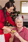 Happy mother offering gift to grandfather at home in the living room