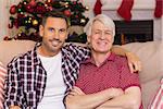 Father with arm around grandfather posing on sofa at home in the living room