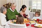 Happy grandfather carving chicken during christmas dinner at home in the living room