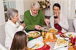 Grandfather carving chicken while women drinking red wine at home in the living room