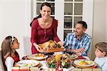 Smiling woman serving roast turkey to her family at home in the living room