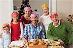 Happy extended family in party hat at dinner table at home in the living room