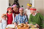 Cheerful extended family in party hat at dinner table at home in the living room