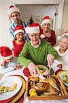 Grandfather in santa hat carving chicken during dinner at home in the living room