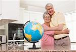 Senior couple smiling at the camera together with globe at home in the kitchen