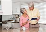 Senior couple shopping online with tablet pc at home in the kitchen