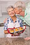 Senior man giving his wife a kiss at home in the kitchen