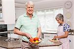 Senior man showing colander of vegetables at home in the kitchen