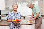 Senior woman showing colander of vegetables at home in the kitchen