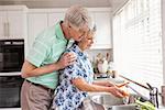 Senior couple washing vegetables at sink at home in the kitchen