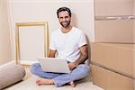 Happy man using laptop surrounded by boxes in his new home