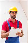 Construction worker taking notes on clipboard in a new house