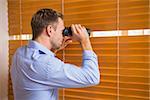 Man looking with binoculars through the blinds in the office