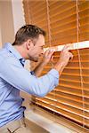 Curious man looking through the blinds at home