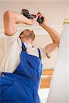 Handyman using a cordless drill to the ceiling in a new house