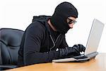 Burglar in sunglasses using laptop on white background