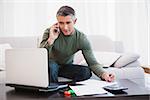 Man with laptop phoning and taking notes at home in the living room