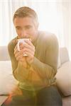 Smiling man drinking hot beverage at home in the living room