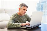 Concentrated man with grey hair using laptop at home in the living room