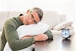 Man resting on cushion with alarm clock on the table at home in the living room