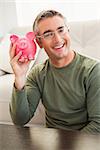 Smiling man posing with a piggy bank at home in the living room