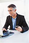 Cheerful businessman using laptop and holding smartphone in his office