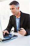 Businessman using laptop and holding smartphone in his office