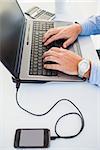 Hands typing on laptop an mobile phone in charge at desk in the office