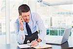 Businessman writing and phoning at his desk in his office