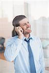 Smiling businessman looking out window on the phone in his office