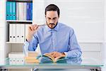 Focused businessman reading book at desk in the office