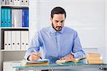 Businessman reading book while writing at his desk in the office