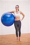 Fit brunette holding exercise ball on wooden floor