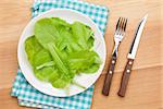 Plate with fresh salad, knife and fork. Diet food on wooden table with copy space