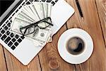 Office table with pc, coffee cup, glasses and money cash. View from above