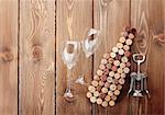 Wine bottle shaped corks, glasses and corkscrew over rustic wooden table background. View from above with copy space