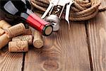 Red wine bottle, heap of corks and corkscrew over rustic wooden table background with copy space