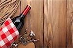 Red wine bottle and corkscrew over rustic wooden table background with copy space