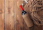 Red wine bottle and corkscrew over rustic wooden table background with copy space